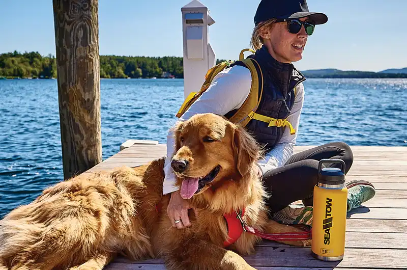 Woman and dog on the dock with a Sea Tow Yeti thermos. Give the gift of a Sea Tow boat tow membership.
